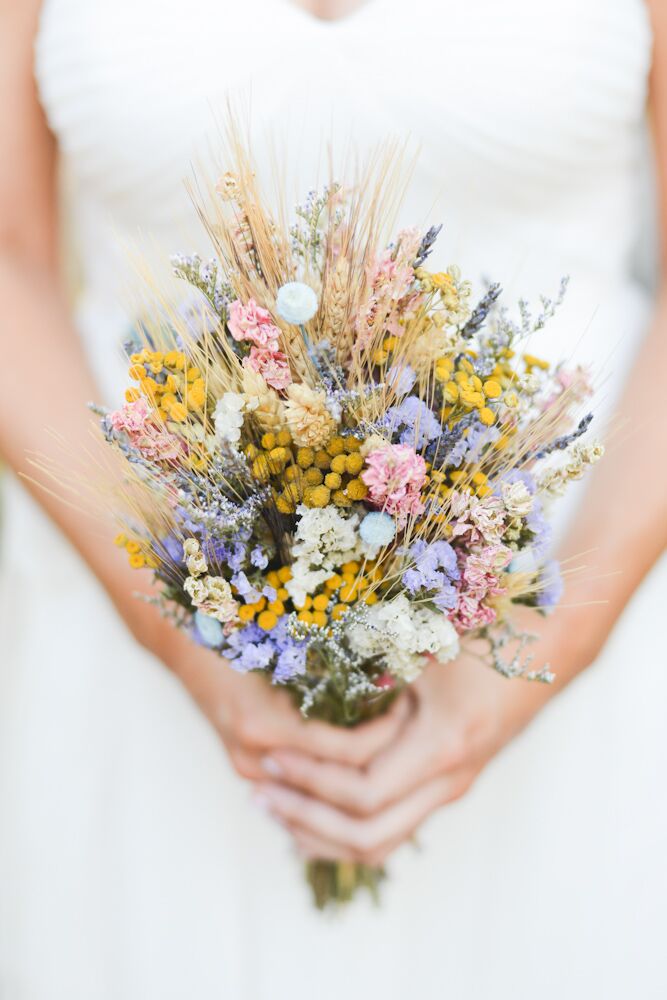 Resembling the rest of their ceremony decor, Stephanie’s pastel bridal bouquet looked like it was just picked from their natural setting. Yellow craspedia, pink delphiniums, lavender and wildflowers all filled its wrap. For an added organic feel, dried wheat popped out throughout the display.
