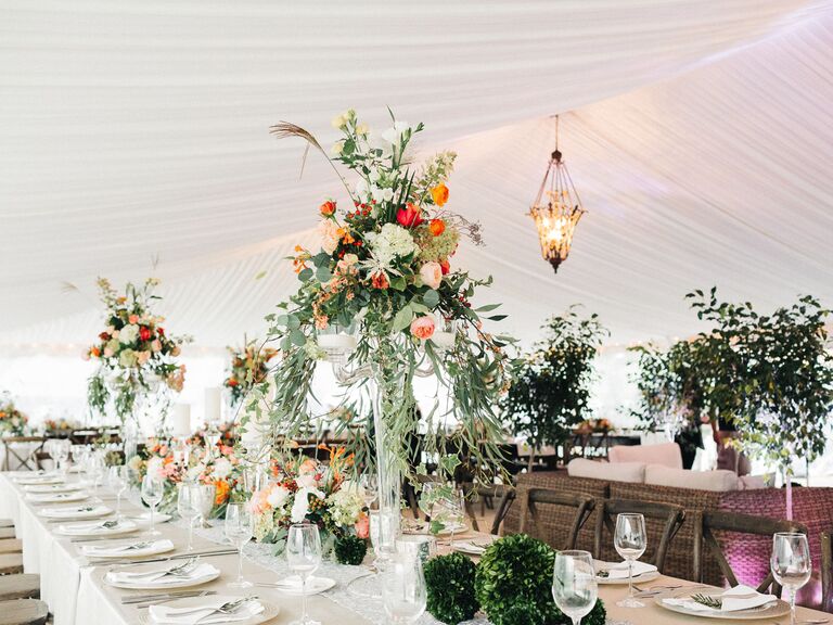 tented wedding reception with tall centerpieces of greenery and orange flowers