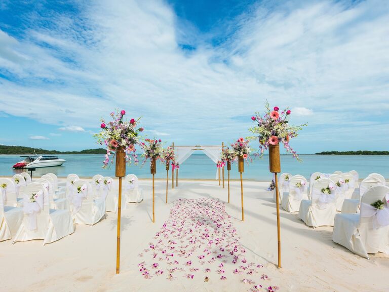 Beach ceremony set up with gorgeous bouquets marking an aisle. 