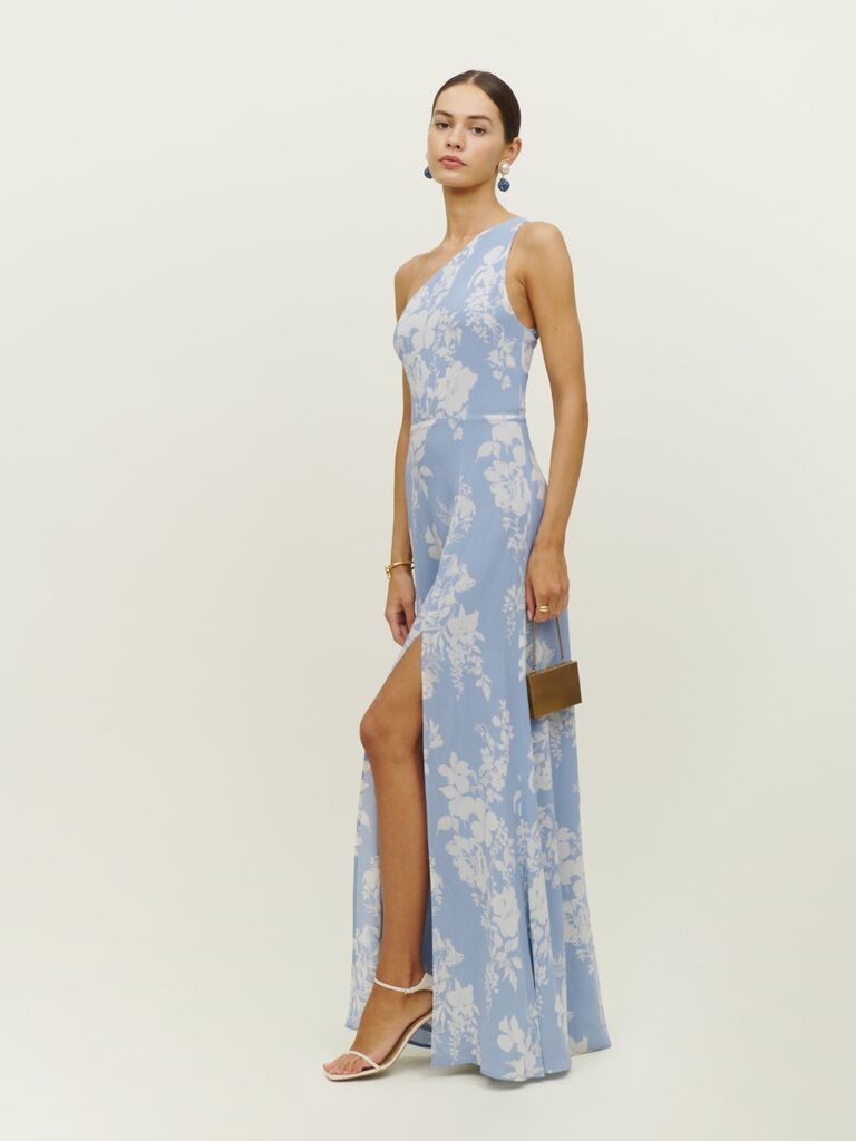 Model wears a one-should sky blue gown with a floral print. 