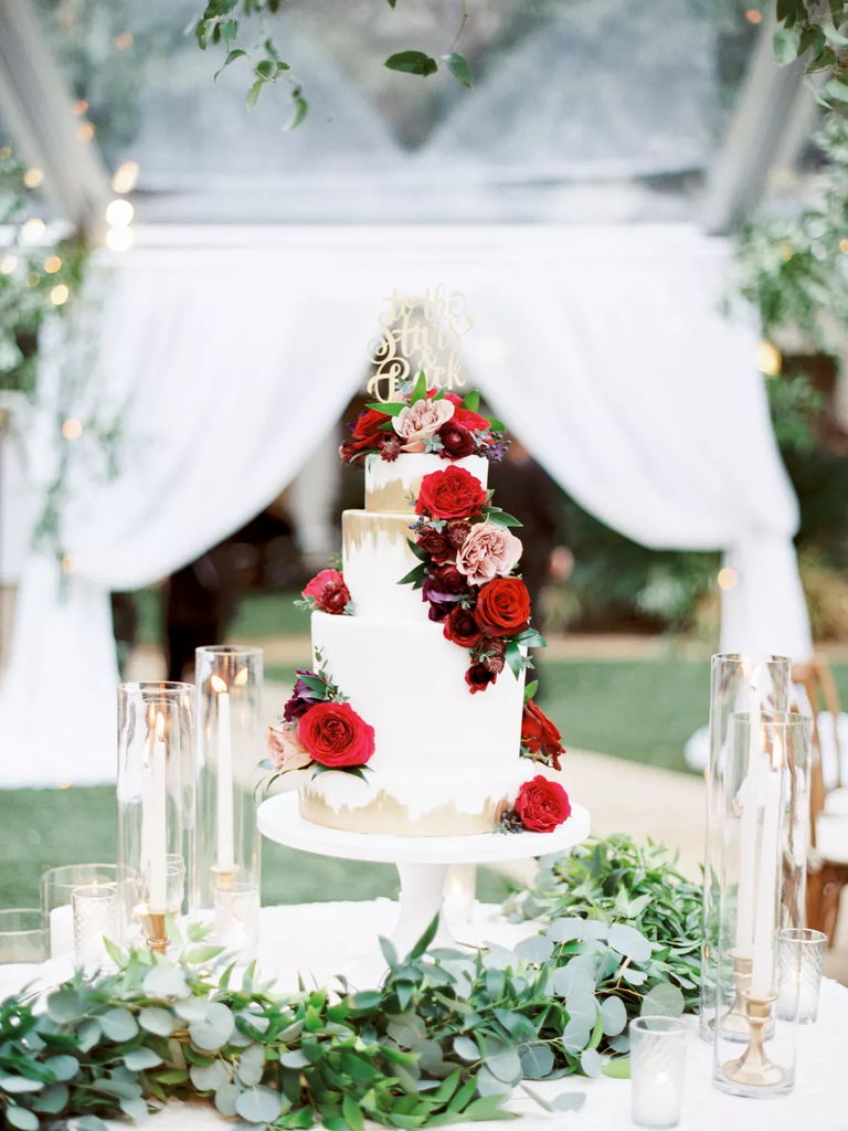 Three-tier white and gold wedding cake with a cascade of red roses