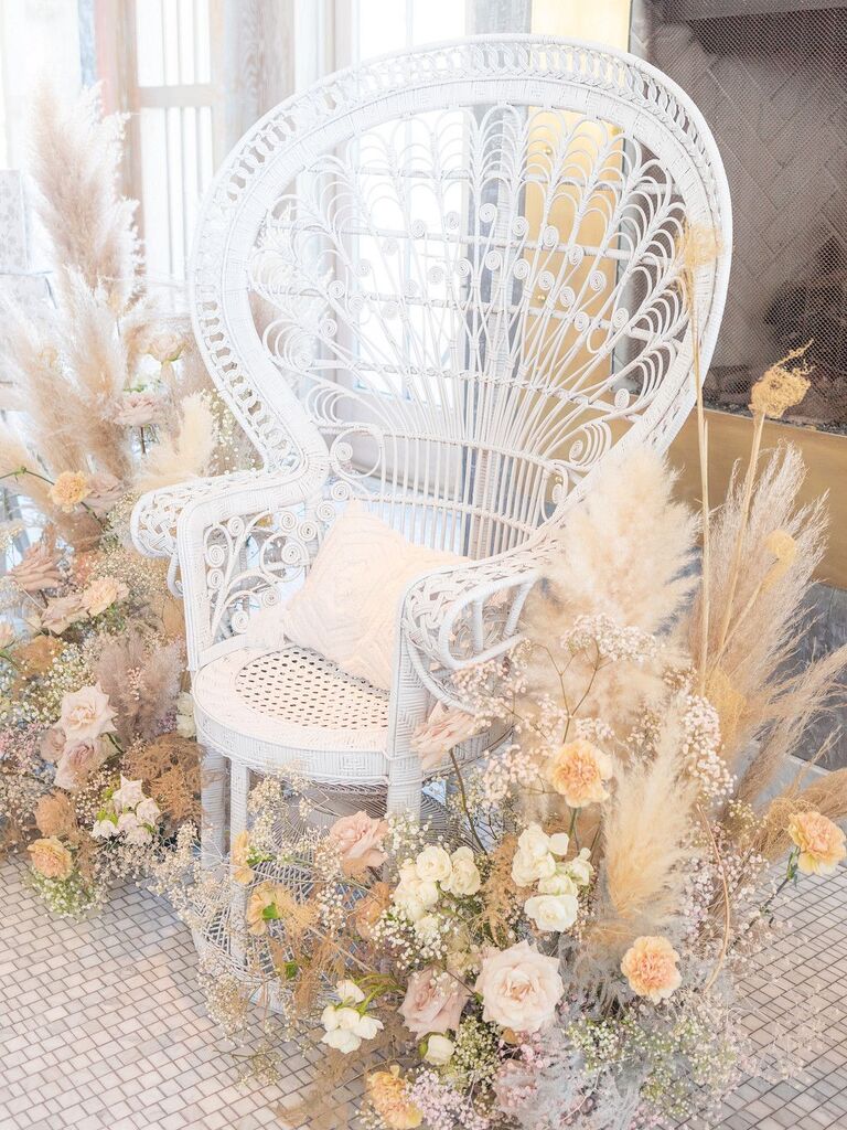 White peacock chair surrounded by pampas grass and peach roses