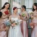 A bride in a sleek A-line gown with detached sleeves and a large bouquet of different pastel flowers posing with her bridesmaids in different satin dresses, all holding varying bouquets of single-flower bunches at a historic venue in Los Angeles.