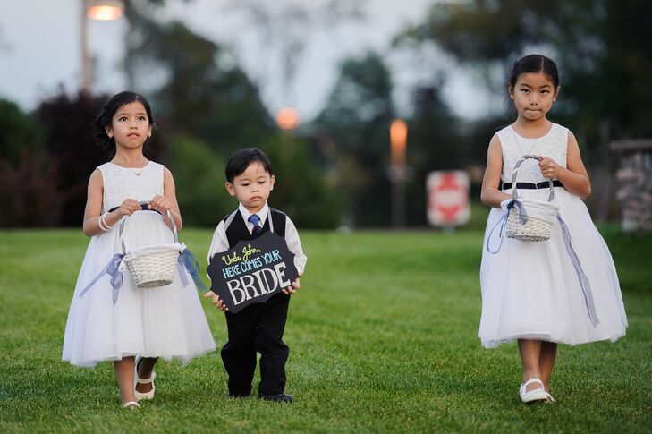 The flower girls wore white dresses and carried white baskets filled with rose petals while John's nephew carried a chalkboard sign that said "Here Comes Your Bride."