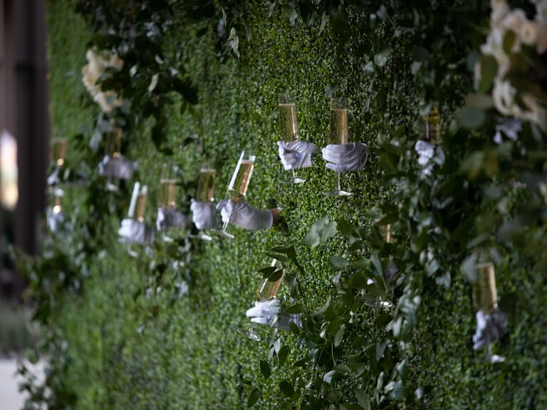 greenery wall with gloved servers passing champagne through windows