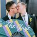 Grooms Kissing, Holding Green, Purple and Yellow Sign With Last Name