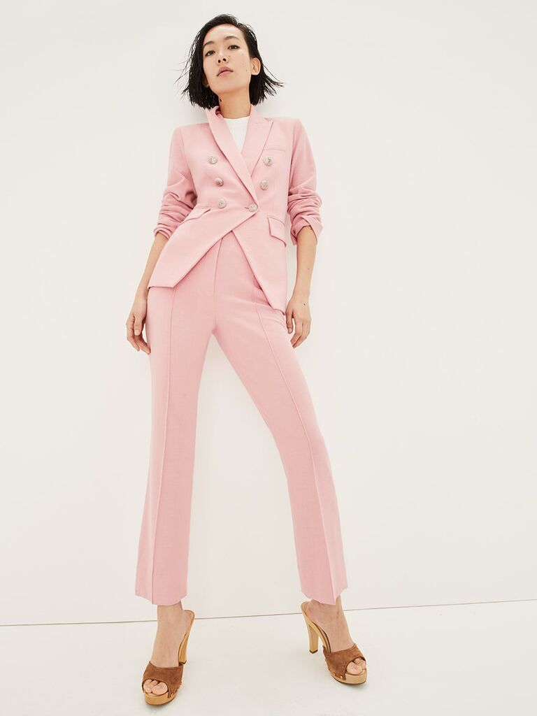 Model wears a blush pink suit set with a cinched waist. 