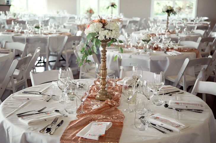 Sparkly blush gold table runners added shimmer to each white dining table, topped with a floral centerpiece of a high or low arrangement of white and pink flowers.
