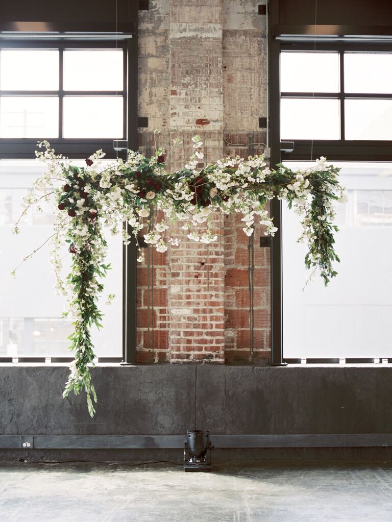 wedding ceremony backdrop with floating flower arch hanging from fishing line in front of old brick wall