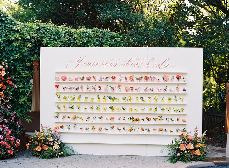Unique, charming escort card display with colorful flowers in hand-painted, custom vases with each guests' name and table number in red, orange, pink and yellow--also acting as wedding favors.