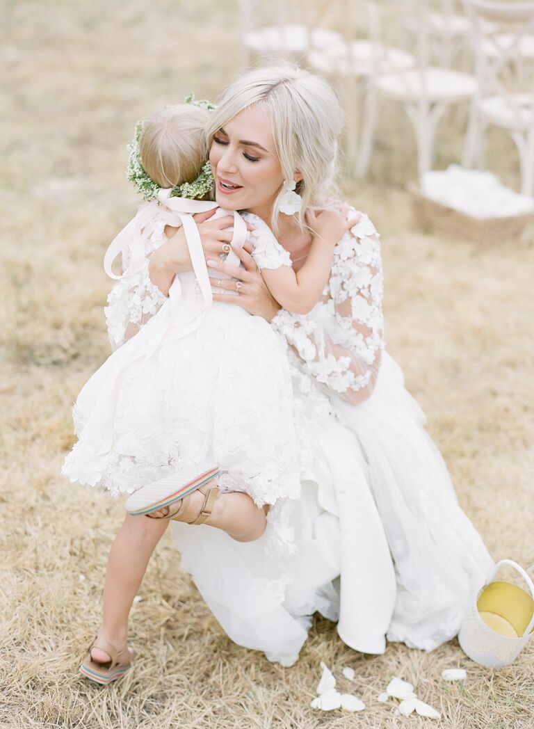 Bride in long-sleeve wedding dress hugging daughter