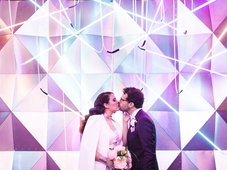 Couple kiss in front of an abstract photo booth backdrop. 