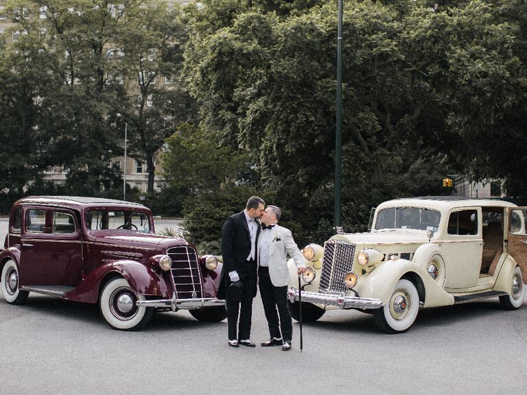Grooms kissing in front of antique getaway cars