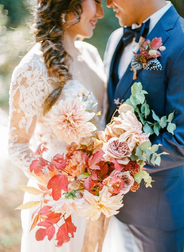 Bride and groom hugging and holding bouquet with leaves and dahlias