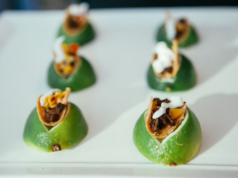 Mini crispy tacos sit on a wedge of lime for a tasty and trendy snack. 