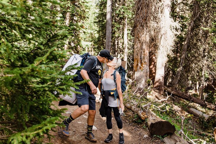 A couple in their casual hiking gear share a kiss as they hike toward their lakeside elopement site in the Rocky Mountains in Colorado.