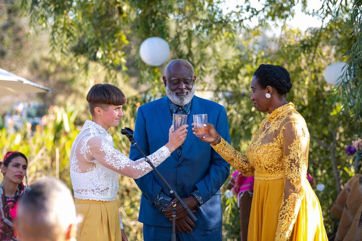 Couple in Yellow Outfits Toasting at Altar During Ceremony With Officiant Under Tree