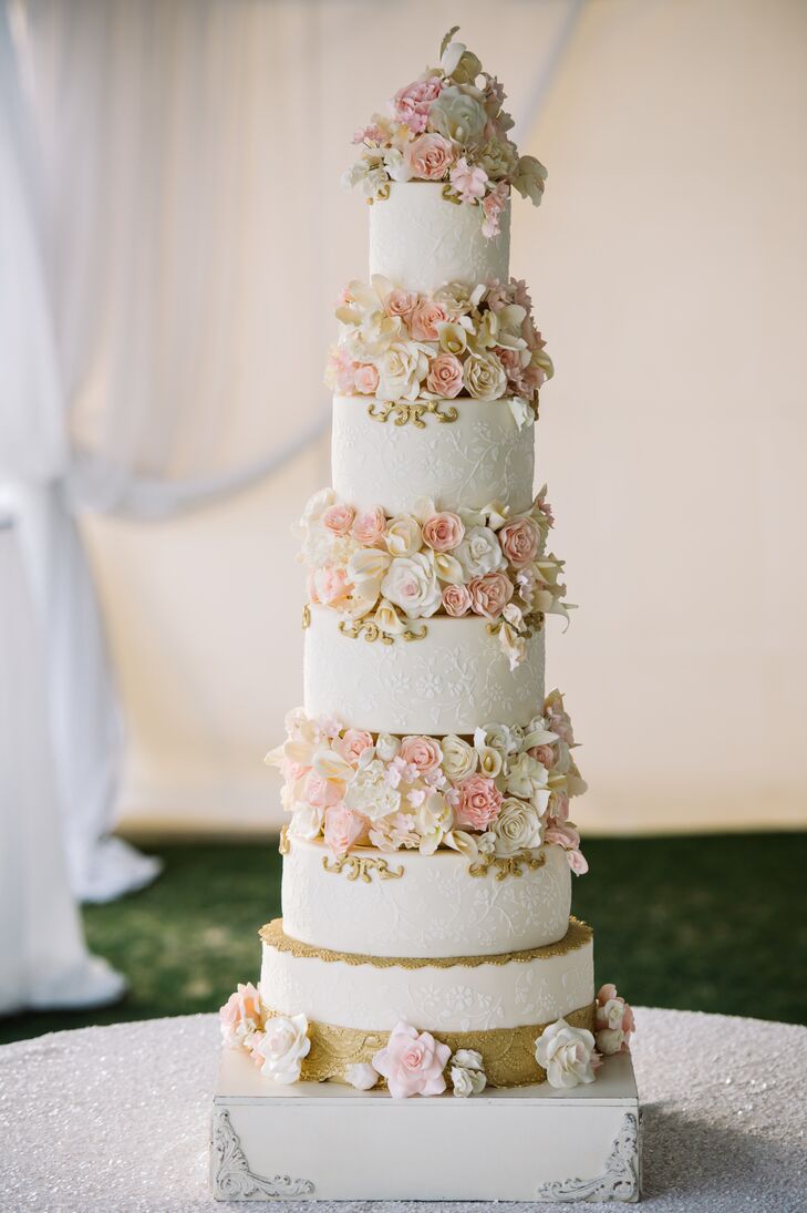 The newlyweds’ towering eight-tier wedding cake alternated layers of satin white fondant with layers of sugar flowers in champagne, blush and cream shades. Embellishments included fondant appliques and lace piping.