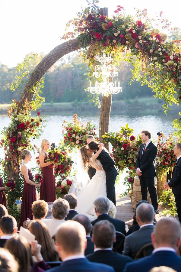 First kiss during lakefront wedding ceremony under arch with chandelier