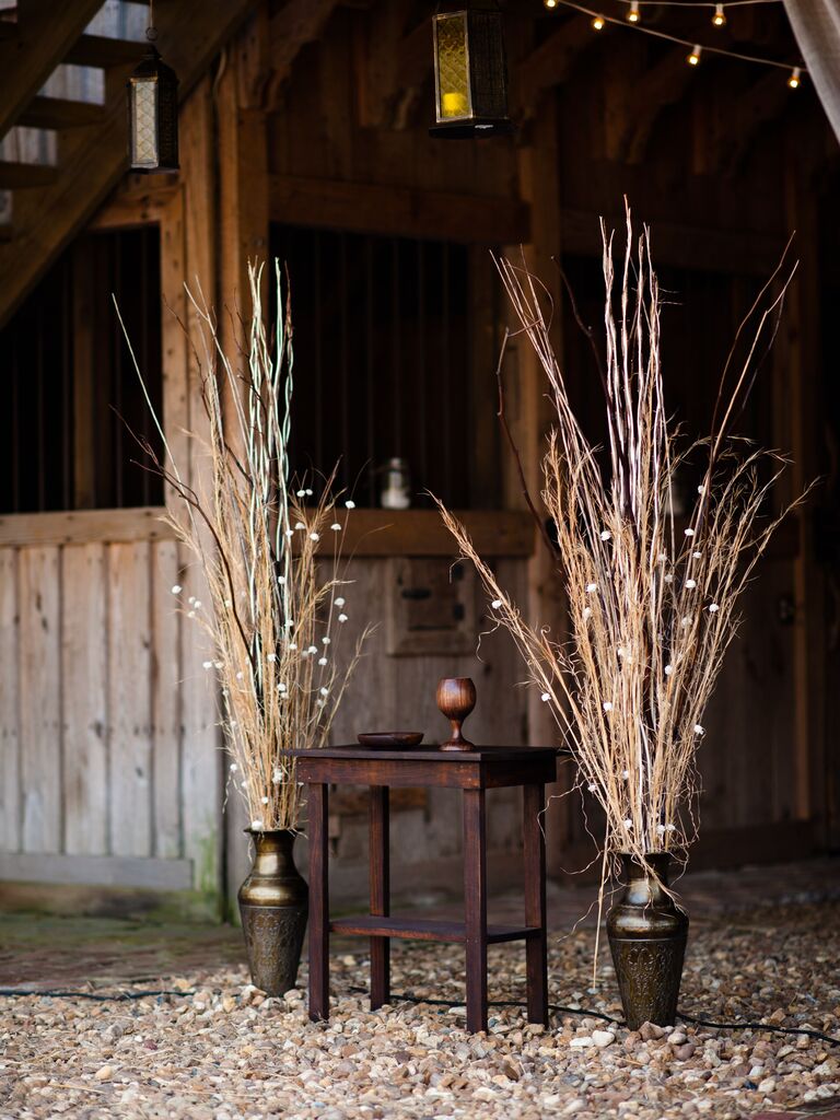 wedding altar decor with tall branches and string lights in bronze urns at rustic barn venue
