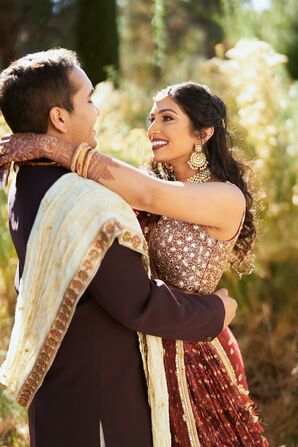 Indian Bride in Dark-Red-and-Gold Attire With Groom in Matching Outfit Embracing