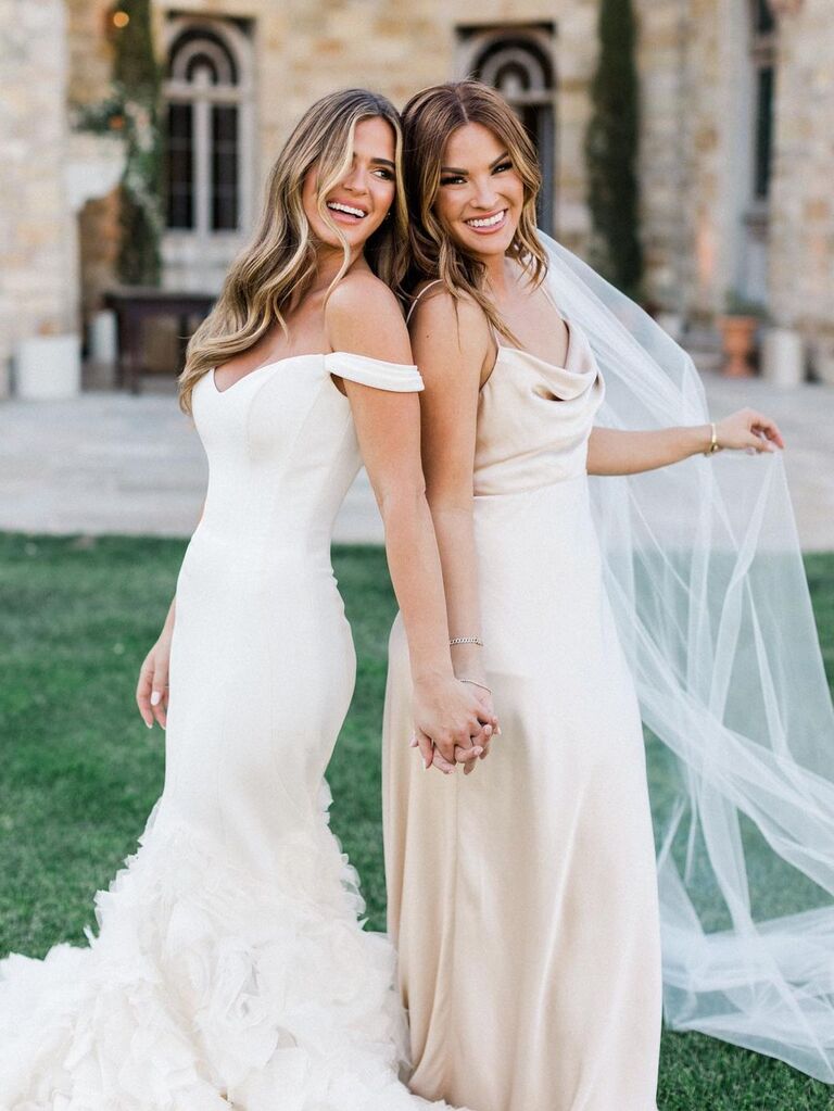Bride and bridesmaid hold hands while smiling for the camera. 