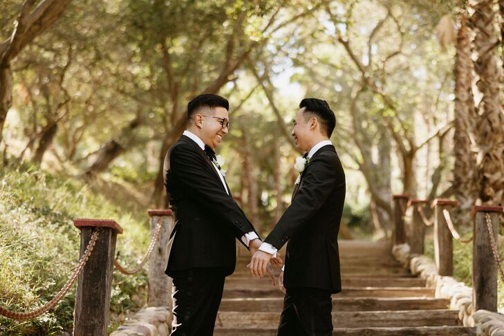 Grooms in Classic Tuxedo Holding Hands on Long, Outdoor Staircase With Trees