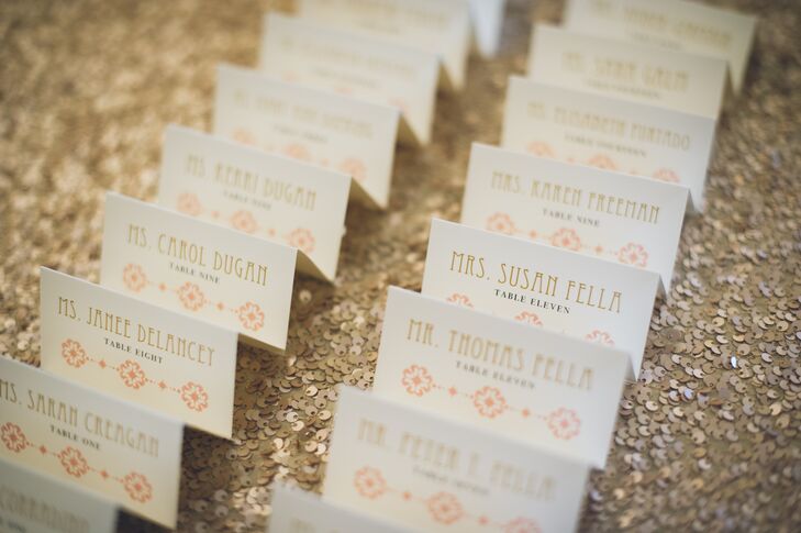 Their escort display incorporated almost every part of the couple’s color scheme as well as their want for “glitzy accents. Placed above a gold sequin linen from La Tavola, each ivory escort card stood out with gold, art deco-worthy font and a geometric peach design. Black table numbers separated the two.