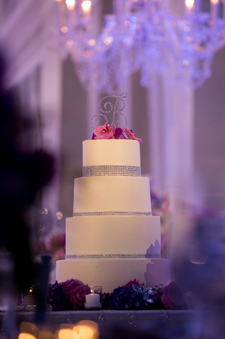 Le Cakery created this four-tier ivory confection. A rhinestone border around each tier echoed the sparkles around the room, and a "B" cake topper tied it all together. A few fuchsia flowers on top added a pop of color.
