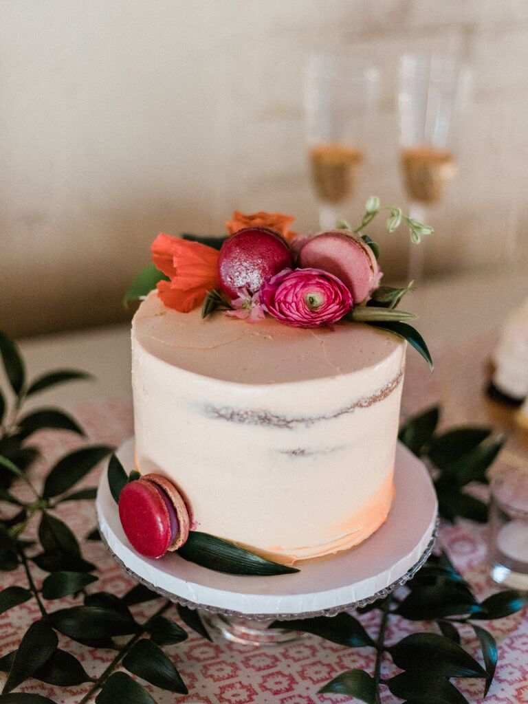 one tier wedding cake with orange ombre frosting, pink and orange flowers and pink macarons