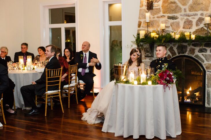 "The hope was to provide a cozy setting where everyone felt comfortable, like a big dinner party,"  Lily says. Their sweetheart table alone resembled just that, with tons of low candlelight and a roaring fire right behind them. Garlands of greenery also lined the space for that homey feel. The gold chiavari chairs, fireplace mantel and sweetheart table were all decorated with the natural accents and some red peonies for an added, rich color.