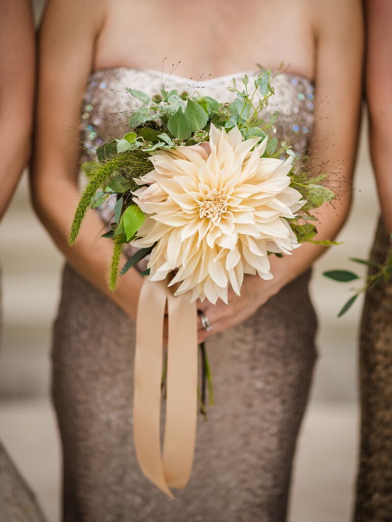 A bridesmaid holds this stunning enormous yellow flower with greenery.
