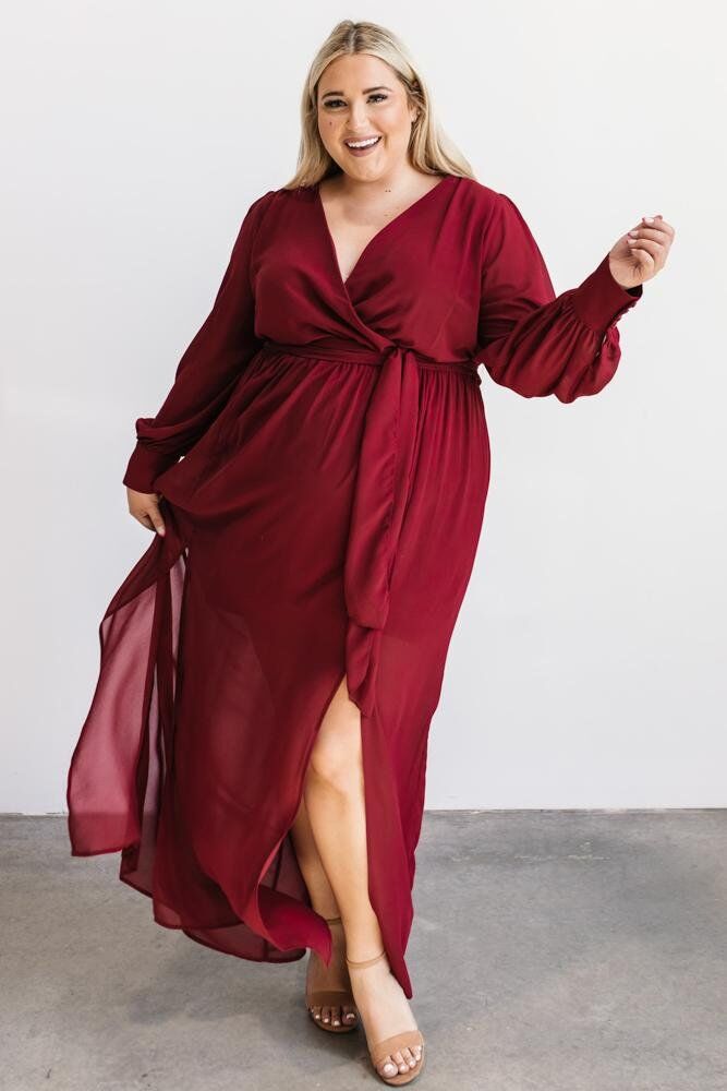 Model wears a long sleeve belted gown in wine. 