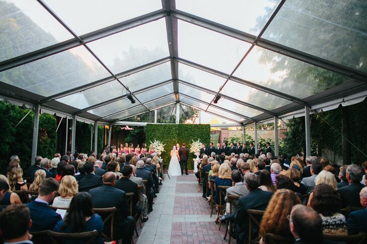 Liz and Dave wed in an outdoor courtyard at Chicago Illuminating Company against a lush backdrop of green ivy and flanked by two large bouquets. "I chose the venue because of the courtyard option and loved that it brought an element of the outdoor to our ceremony," the bride says. Guests watched on while seated on white, wood grain chairs.