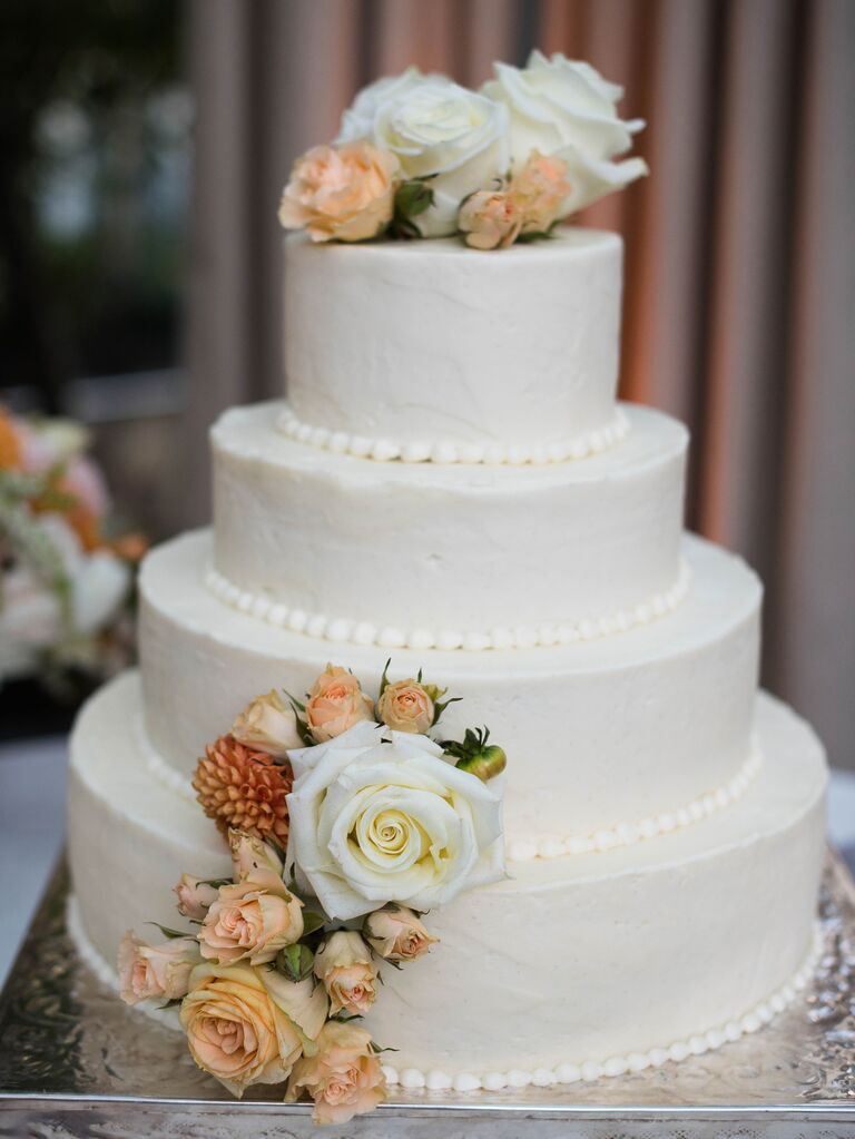 four tier white wedding cake with beige and ivory roses and hand-piped trimming