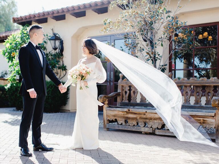 Bride and groom posing with bride's long veil blowing in the wind