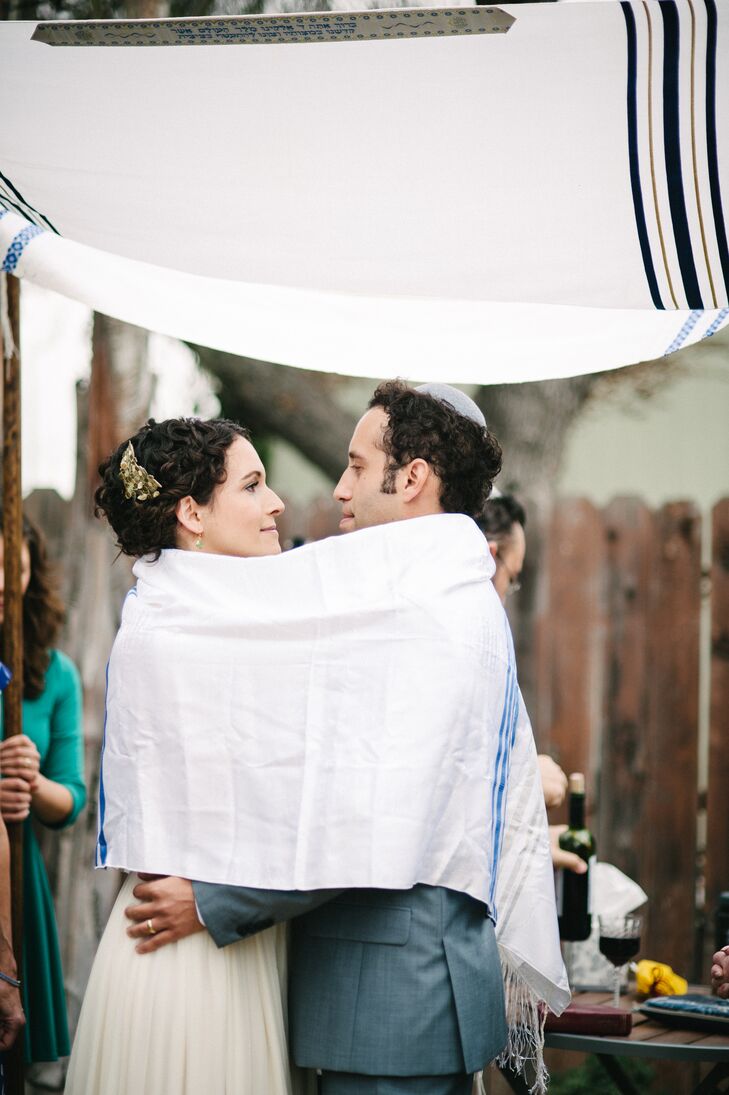 Emily and Chris were wrapped by the tallith during their Jewish ceremony, which took place under their white and blue chuppah. Instead of four poles holding up the Jewish prayer shawl, the couple chose four close family members to hold up the poles, incorporating loved ones into their ceremony.