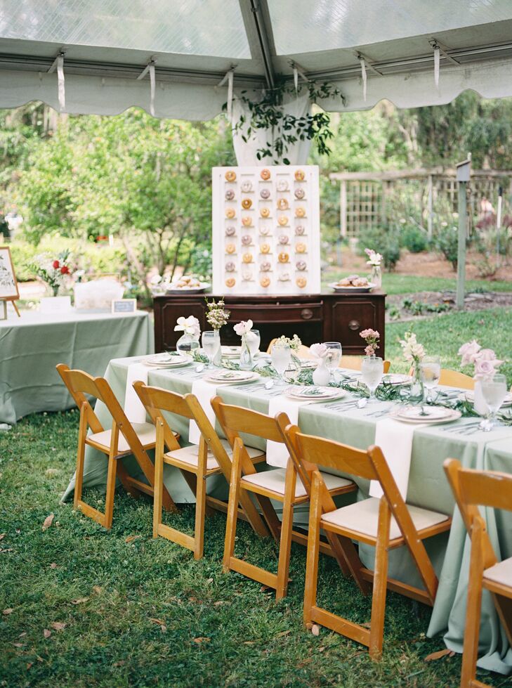 A couple's simple and vintage reception design under a gazebo featuring lots of greenery, pastel flowers, and a donut wall in a botanical garden setting.