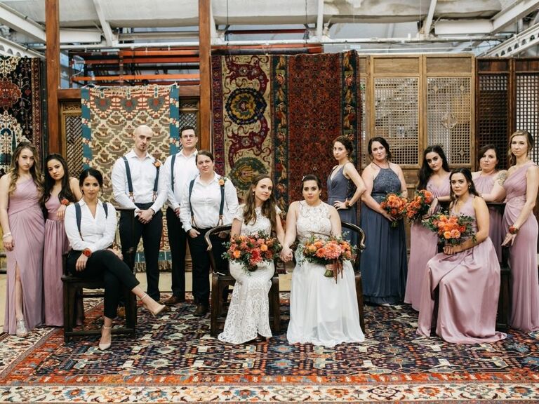 brides posing with wedding party in eclectic venue decorated with vintage rugs