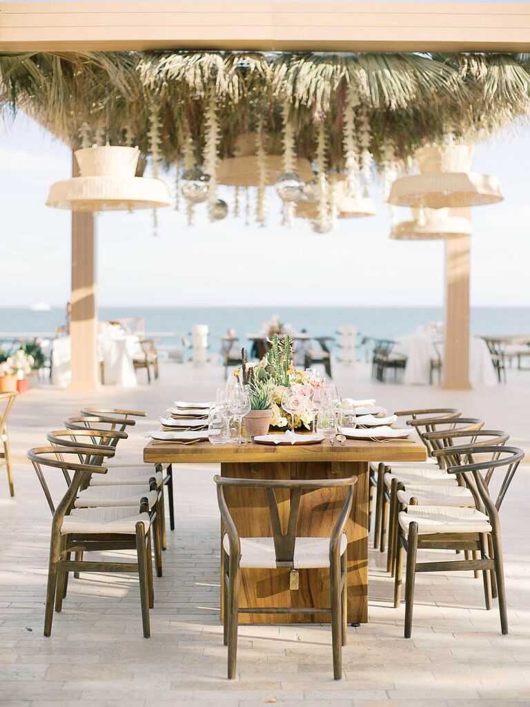 Beachfront wedding reception with large chandeliers and hairpin chairs