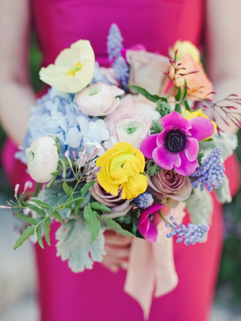 A bridesmaid holds this vibrant yellow, blue, and pink bouquet.