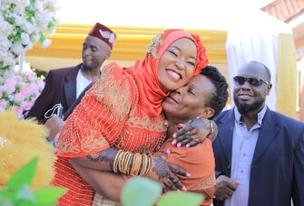 Smiling Ugandan couple embrace while loved ones look on.