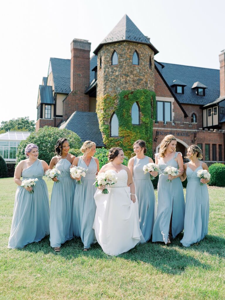 Bride surrounded by her bridesmaids who wear light blue gowns in various styles. 
