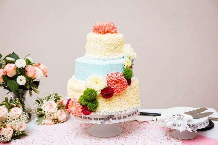 The wedding cake was iced with blue and yellow frosting, and then decorated with dahlia, chrysanthemum and moss balls. The cake was positioned on a stand ned to the serving set.