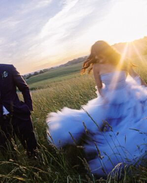 Bride in Ruffled Blue Wedding Dress Running Through Field at Sunset