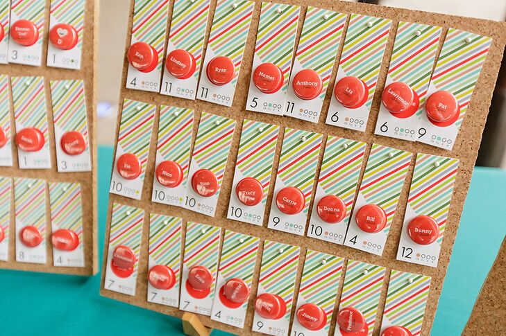 Escort cards were hung on a board for guests to find their table number, designed in red, green and neutral hues with a bright red pin.