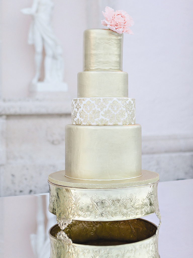 Four tier gold wedding cake topped with a light pink peony
