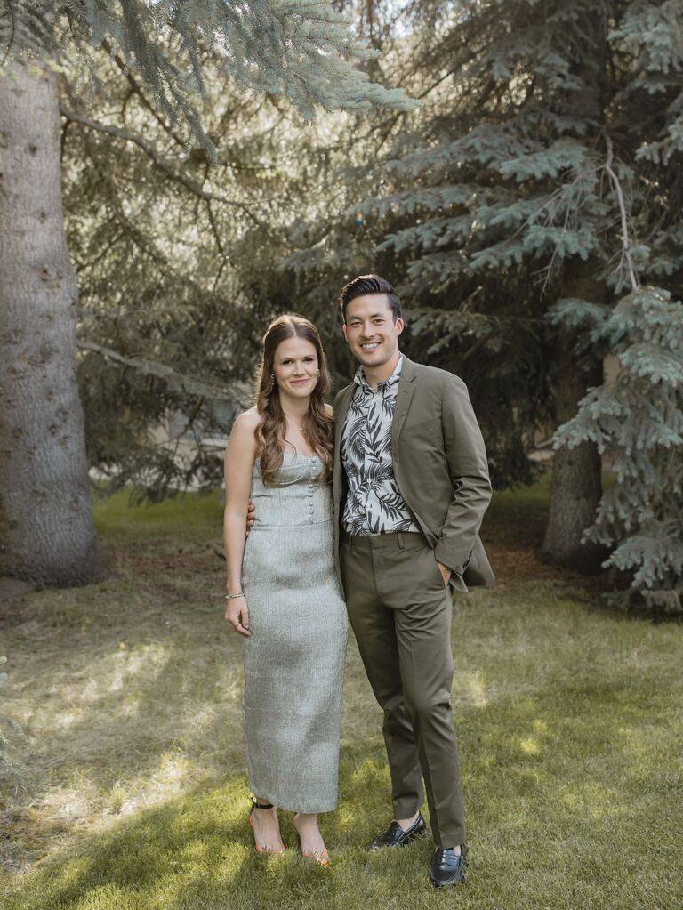 The couple smile for the camera outdoors among the trees