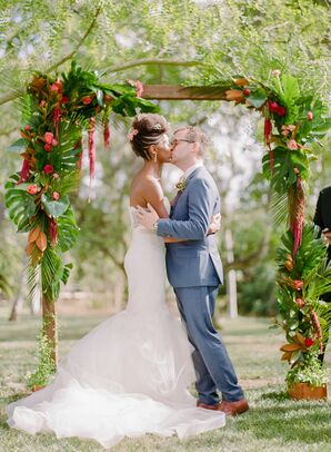 First Kiss Under Wedding Arch Covered in Tropical Leaves