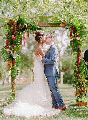 First Kiss Under Wedding Arch Covered in Tropical Leaves